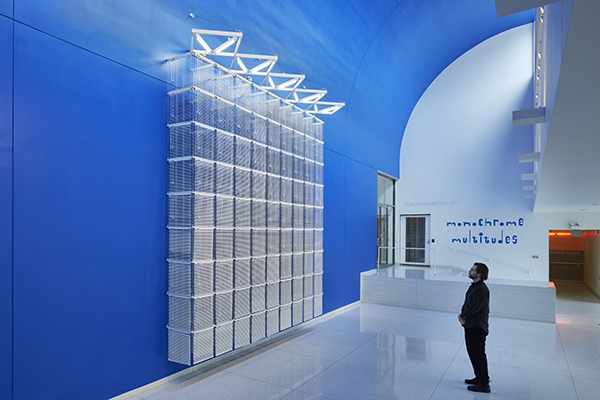 A grid of white blinds are suspended against a blue wall