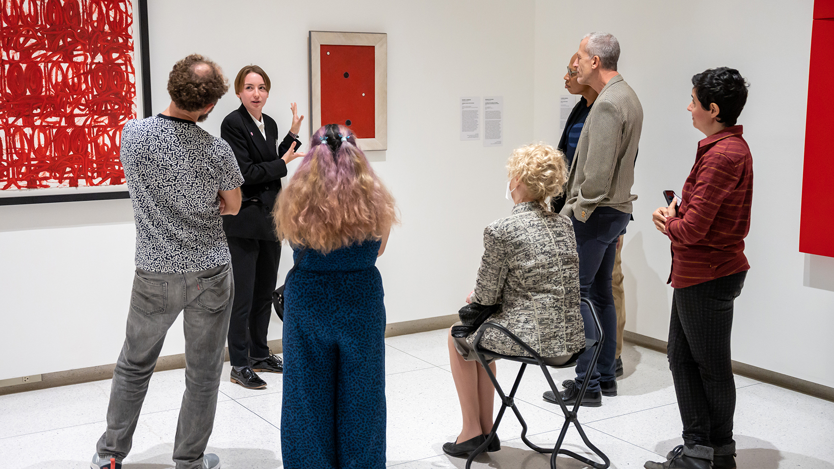 A small group gathers for a gallery talk, surrounded by red abstract paintings